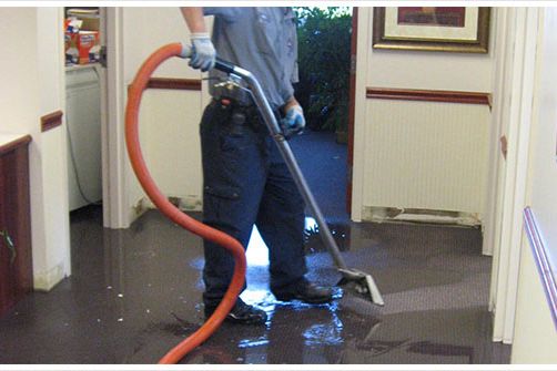 Worker using a wand extractor to remove standing water from a flooded interior floor